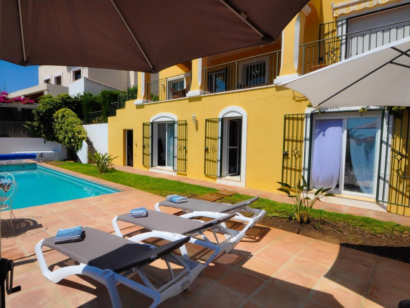 Ein gelbes Gebäude mit Pool, Außenbereich und überdachter Terrasse.