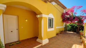 Un edificio amarillo con un patio adoquinado, una puerta blanca y una ventana con rejas.