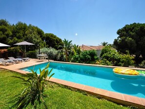 A rectangular swimming pool with a tiled edge, surrounded by a grassy area and trees. There are lounge chairs and umbrellas near the pool. - Cosy holiday home with private pool in Salobreña (Salobreña)