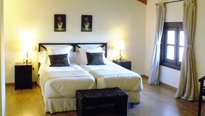 Une chambre avec deux lits, des poutres apparentes en bois au plafond, une fenêtre avec des rideaux et des lampes de chevet.
