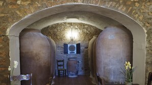 Une cave à vin rustique avec des murs en pierre, de grands tonneaux et une table en bois entourée de chaises.