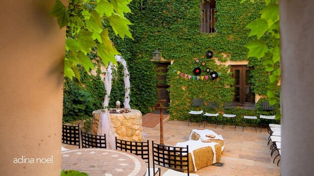 Un espace extérieur aménagé en terrasse, doté d’un sol en pierre, de tables et de chaises blanches, et entouré d’une végétation luxuriante et de murs couverts de lierre.