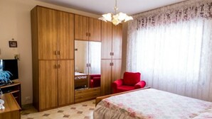 Ein Schlafzimmer mit einem Bett, einem Kleiderschrank, einem roten Sessel und einem Fernseher.