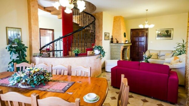 Ein geräumiger Wohnbereich mit einem Holzespeisetisch, der für eine Mahlzeit gedeckt ist, einem roten Sofa und einer Treppe, die zu einer oberen Ebene führt.
