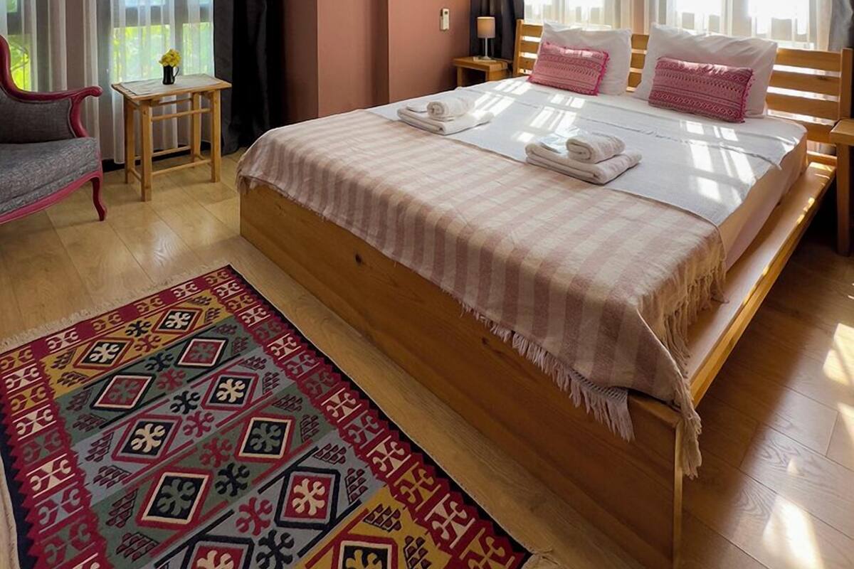 A bedroom with a large bed, a bedside table, a lamp, and a window with curtains.