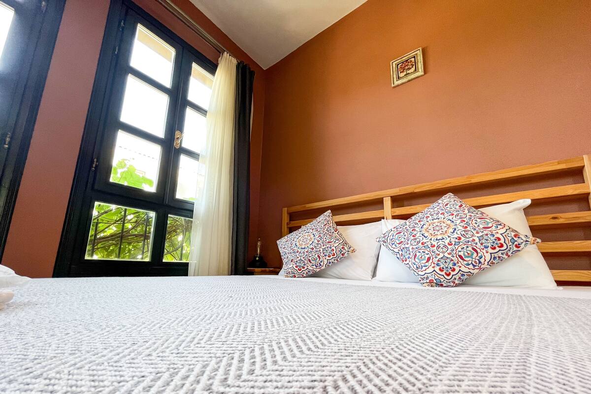 A hotel room with a large bed, a wooden headboard, and a window with curtains.