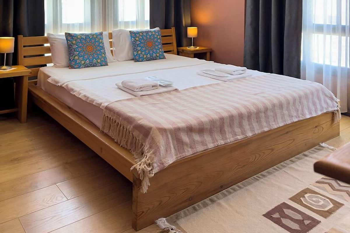 A bedroom with a wooden bed, two bedside tables, a hanging lamp, and a large window with curtains.
