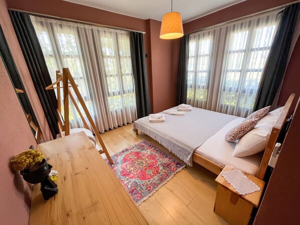 A bedroom with a bed, a wooden table, a hanging light fixture, and a window with curtains.