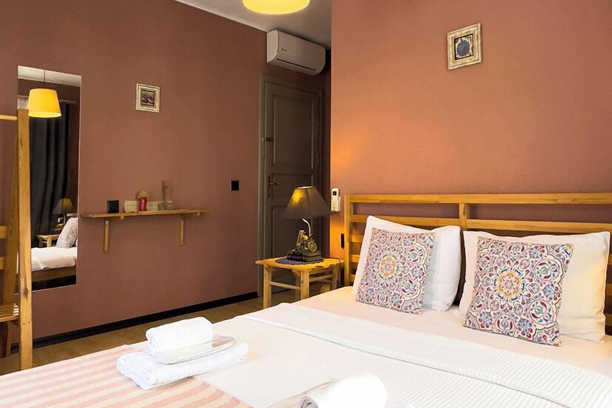 A hotel room with a large bed, a wooden headboard, a bedside table with a lamp, and a mirror.