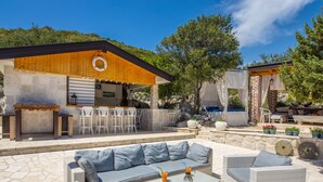 An outdoor patio with wicker furniture, a bar area, and a stone-tiled floor. - Etno House Wagner (Peracko Blato)
