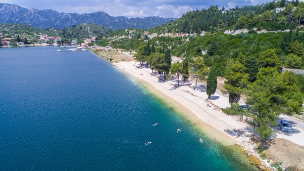 A coastal area with a beach, clear blue water, and a mountainous backdrop. - Etno House Wagner (Peracko Blato)