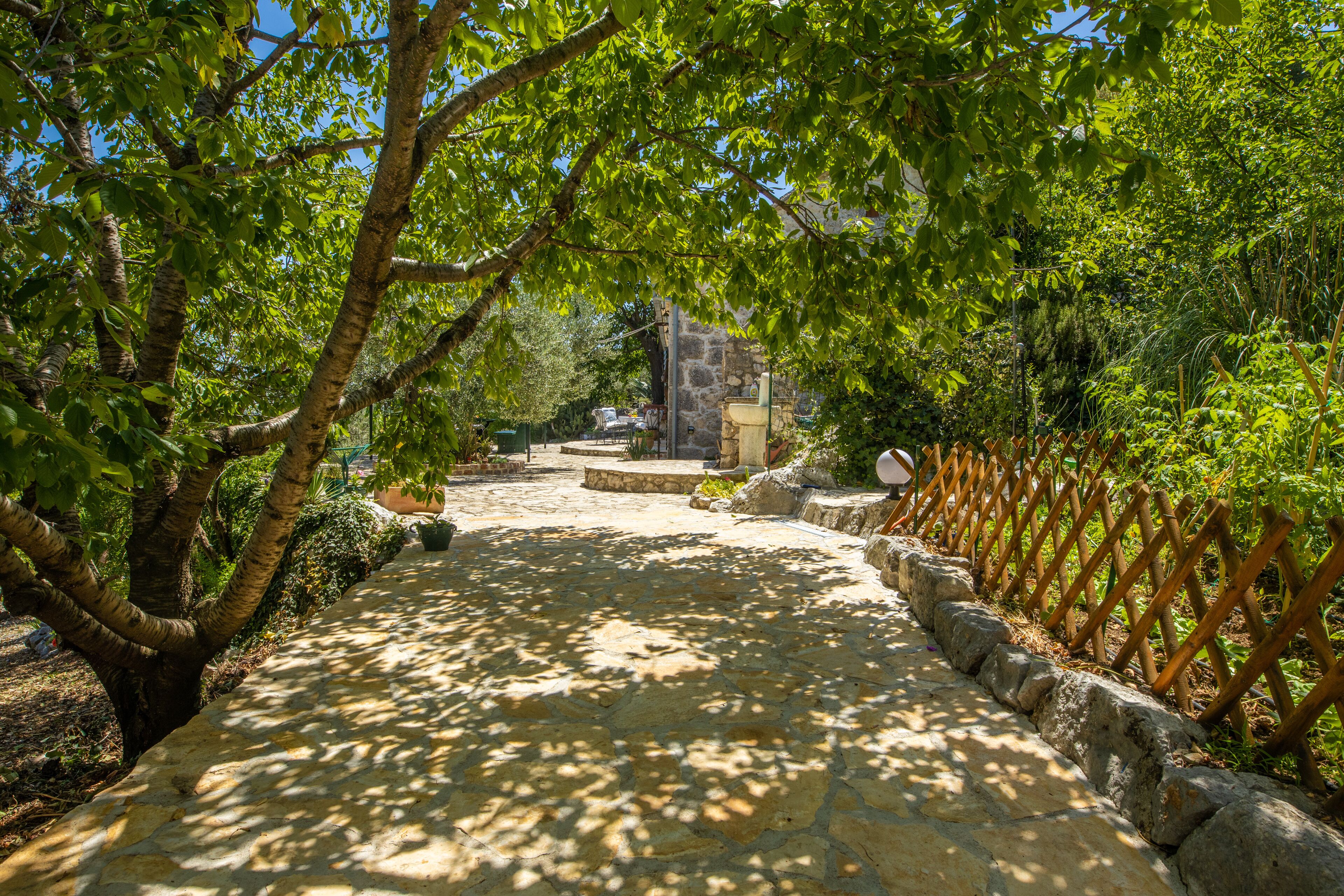 Un chemin de pierres menant à un bâtiment en pierre, entouré d’arbres et d’une clôture en bois.