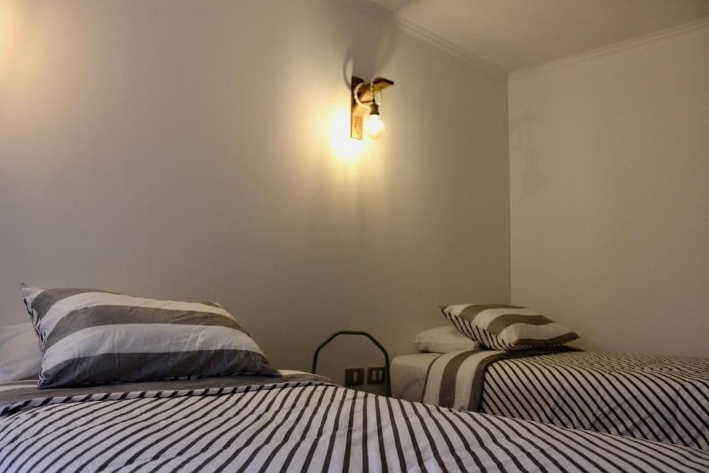 A hotel room with two beds, striped bedding, a wall-mounted light fixture, and a simple, clean design.