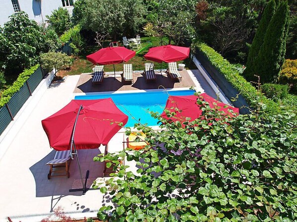 A swimming pool area with red umbrellas, lounge chairs, and a view of the surrounding greenery.