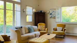 A spacious living room with a large arched window, a sofa, two armchairs, a coffee table, and a wooden cabinet.