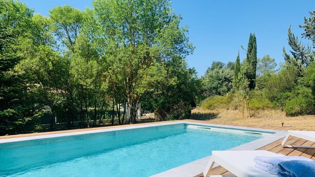 A rectangular swimming pool with a wooden deck and lounge chairs.