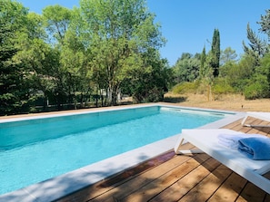 Una piscina rectangular con terraza de madera y sillas de descanso.