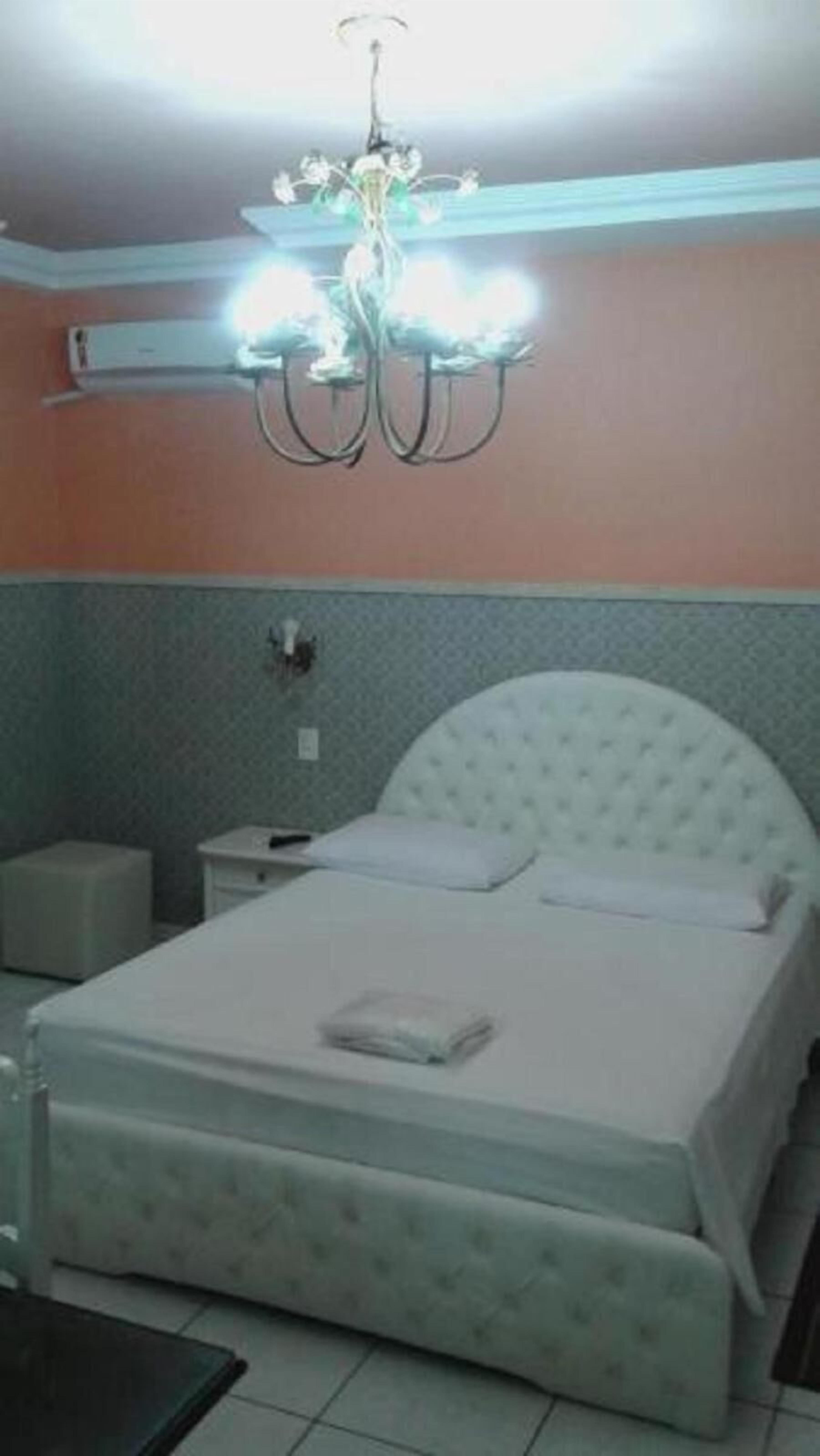 A bedroom with a bed, a nightstand, a bedside table, and a chandelier.