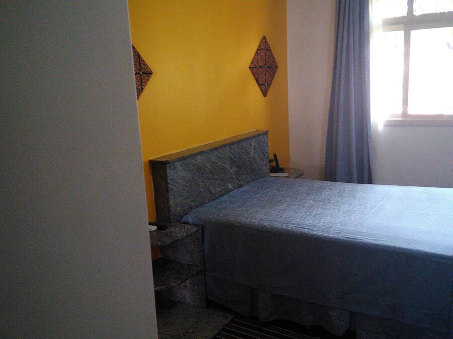 Una habitación pequeña y sencilla con una cama, una ventana con cortinas y una pared con diseño geométrico.