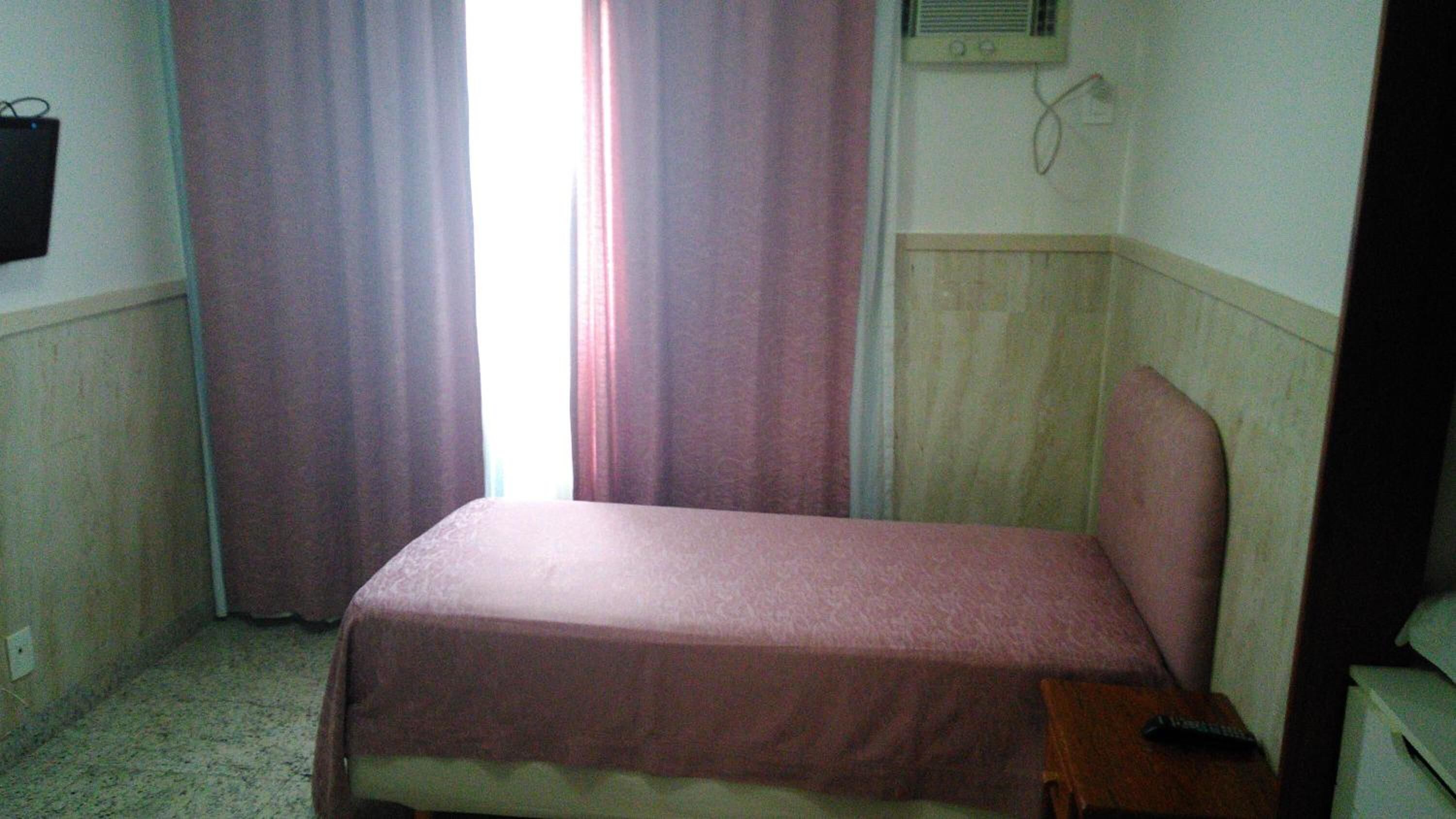 Una habitación pequeña con cama individual, una mesita de noche y un calefactor en la pared.