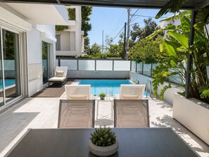 Een modern zwembad met een glazen balustrade, ligbedden en potplanten.
