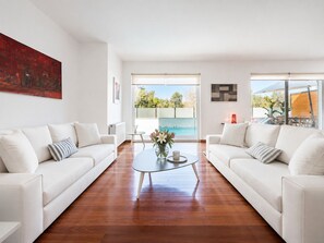 Una sala moderna con dos sofás blancos, una mesa de centro de vidrio y vista a una piscina.