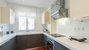 A modern kitchen with a built-in oven, a stainless steel range hood, and a window with a view of greenery. - Welcome to Lumen Villa the first of the Adelos Trilogy (Elliniko)