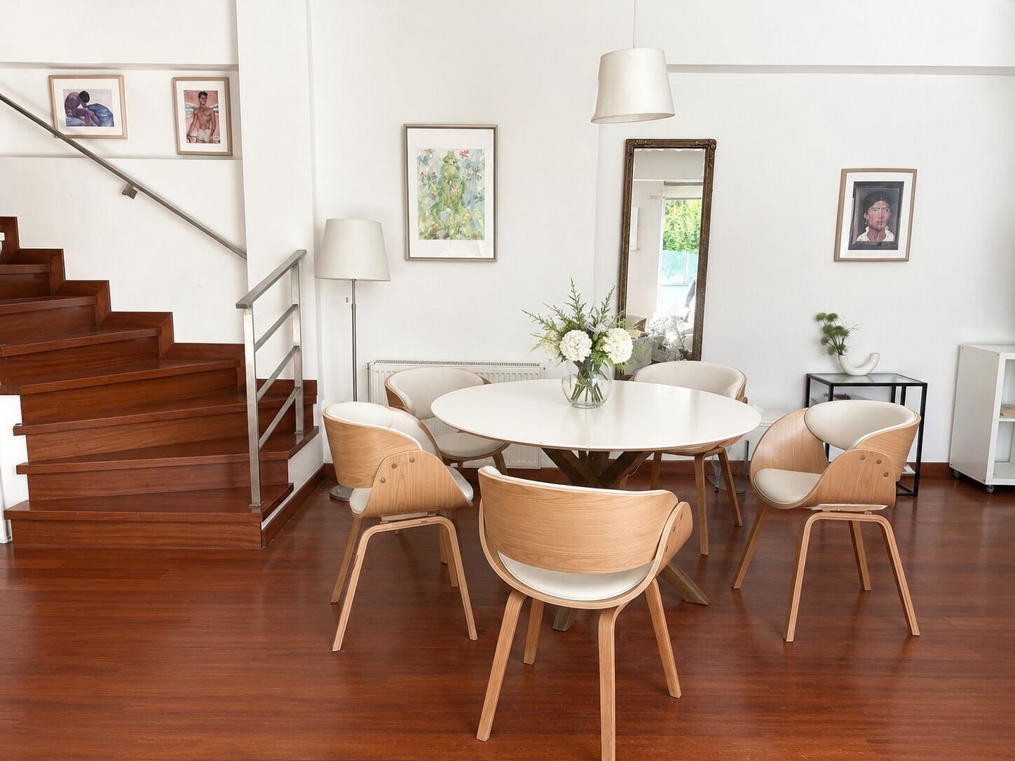 A modern dining area with a round table, six chairs, and a vase of flowers.
