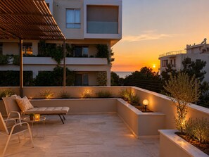 Ein moderner Außenbereich mit Sitzgelegenheiten, darunter eine Couch und Stühle, umgeben von Pflanzen und Blick auf einen Sonnenuntergang.