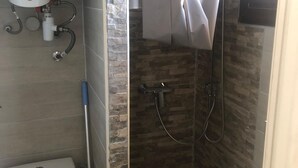 Une petite salle de bain comprenant des toilettes, une douche avec un mur en pierre et une fenêtre avec un rideau.