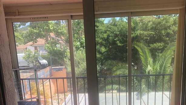 Un balcon donnant sur un quartier résidentiel, un sol carrelé et un canapé rouge.