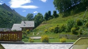 Eine Terrasse mit Steinboden, Holzzaun und Blick auf einen Berg und Grünflächen.