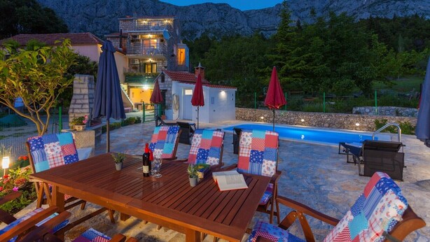 A wooden table with chairs, a pool, and a mountain backdrop. - Villa Paradise village in Tucepi, private pool (Tucepi)