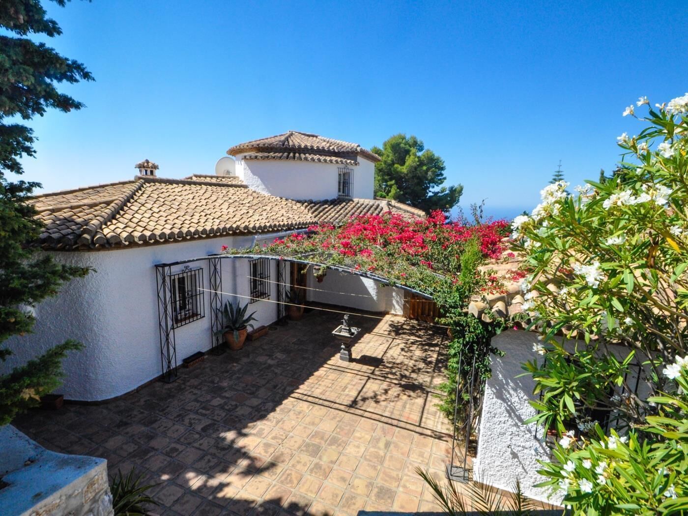 A courtyard with a tiled roof, potted plants, and flowering bushes.