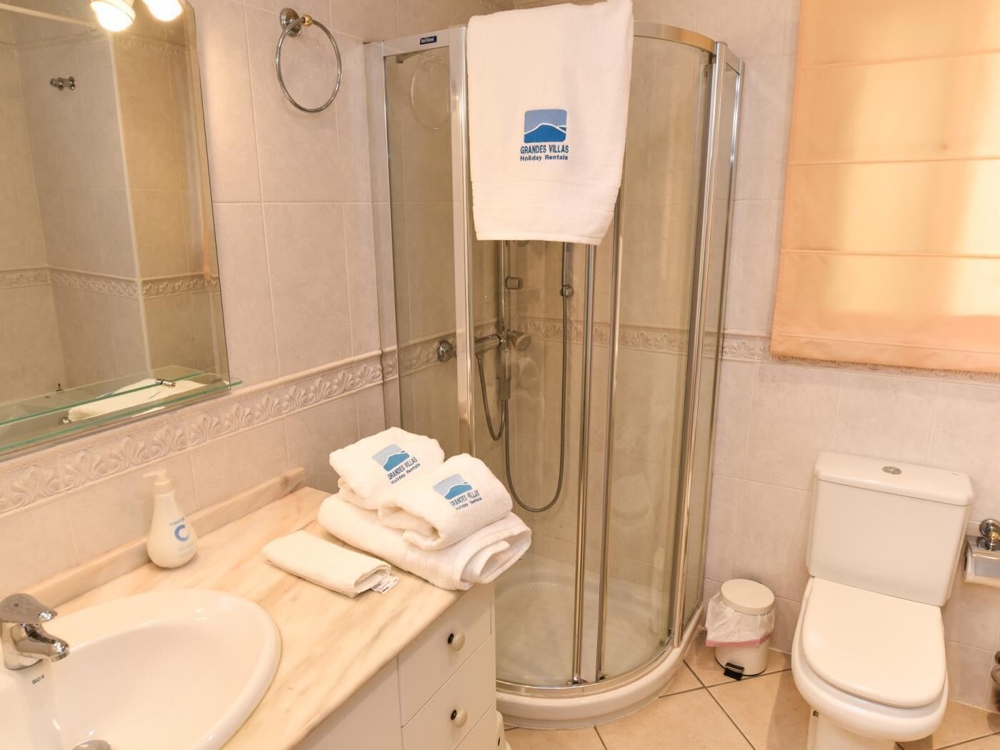 Une salle de bain avec une douche à parois de verre, un lavabo avec un miroir et des toilettes. Des serviettes et des articles de toilette sont posés sur le comptoir.