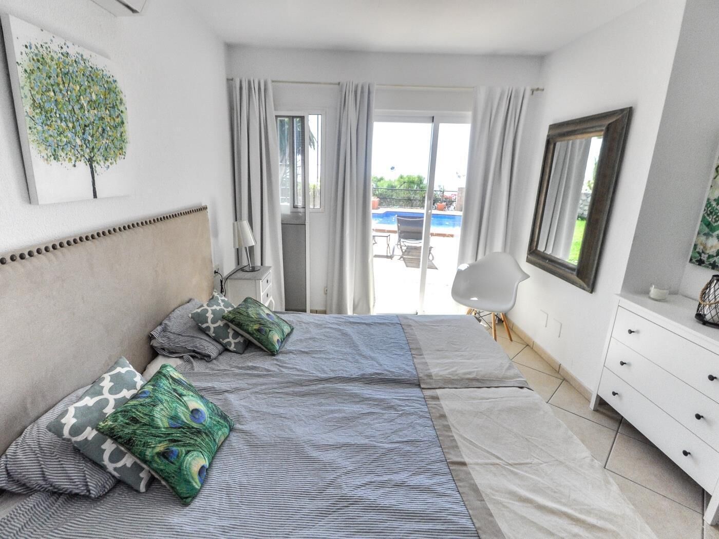 A bedroom with a bed, a dresser, a chair, and a view of an outdoor swimming pool.