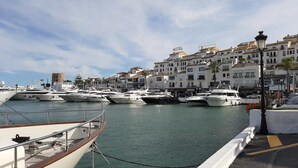En lysthavn med flere sejlbåde i havnen, et hotel ved navn "HOTEL" i baggrunden, og en kystby med hvide bygninger.