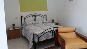 Ein Schlafzimmer mit einem Bett, einem Nachttisch, einem Beistelltisch, einem Sessel und einem Wandbild.