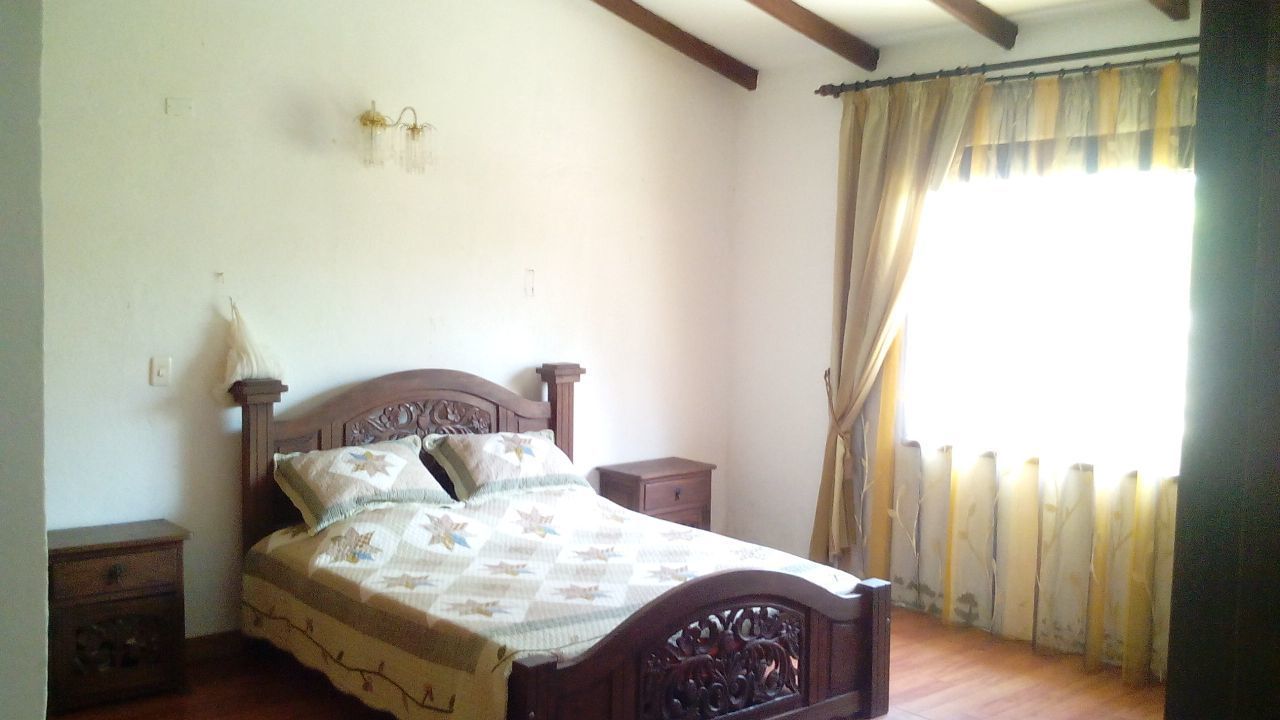 Un dormitorio con cama de madera, una mesita de noche, una lámpara y una ventana con cortinas.