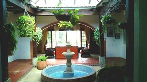 Pátio com fonte, plantas pendentes e área de estar com cadeiras.