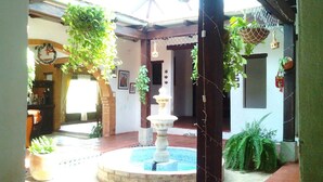 Um pátio com uma fonte central, plantas em vasos e folhagem pendente.