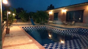 A swimming pool with checkered tiles, a slide, and outdoor seating.