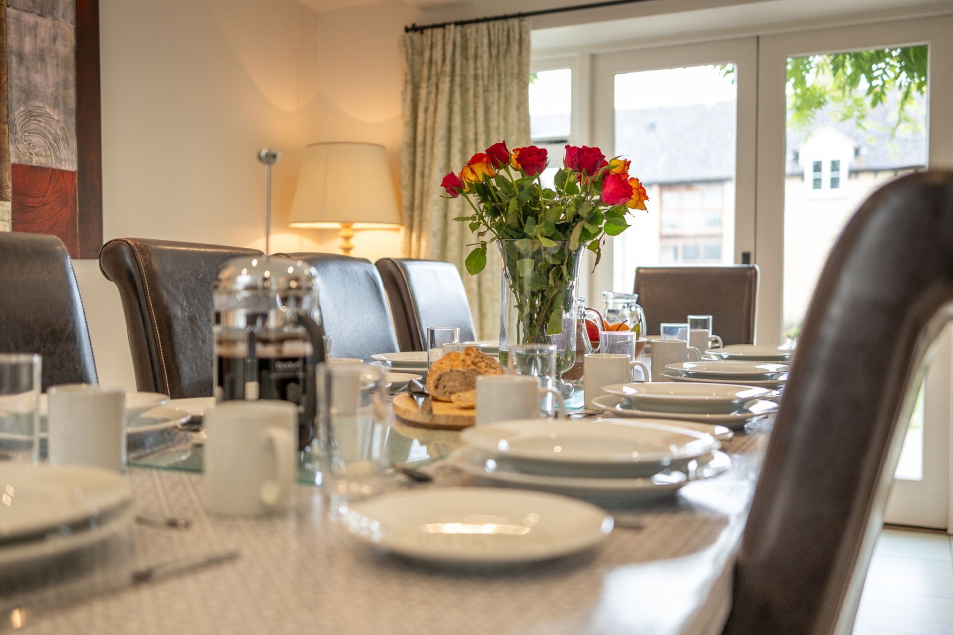 Een eettafel gedekt met borden, glazen en een bloevas.