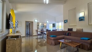 A spacious living area with a brown sectional sofa, a wooden coffee table, and a dining table with chairs. There is a large mirror on the wall, a flat-screen TV, and a decorative silver vase. - Apartment Penthouse by the sea - Vrboska - Island Hvar (Vrboska)