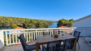 A balcony with a wooden table, chairs, and a view of a lake and forest. - Apartment Penthouse by the sea - Vrboska - Island Hvar (Vrboska)