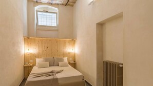 Een slaapkamer met een houten hoofdbord, een bed met een beige dekbedovertrek, twee nachtkastjes met lampen, een radiator en een raam met een rasterpatroon.