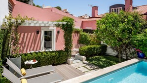 A poolside area with a wooden deck, a small table with a vase, and a white chair. - By the Castle | LUXURIOUS, PRIVATE GARDEN & HEATED SWIMMING POOL (Lisboa)