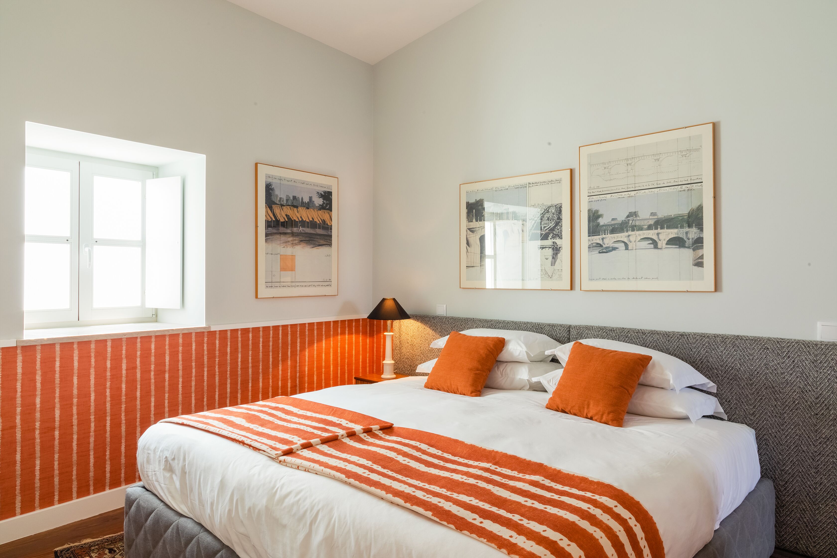 A hotel room with a bed, a window, and two framed pictures on the wall.