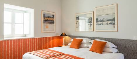 A hotel room with a bed, a window, and two framed pictures on the wall.