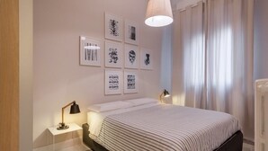 Ein modernes Schlafzimmer mit einem Bett, Nachttischlampen, einem klaren Nachttisch und einer Wand mit gerahmten Kunstwerken.